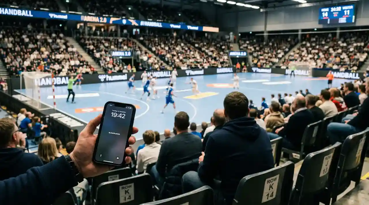 Person hält ein Smartphone während eines Handball-Spiels in der Arena